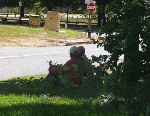 Men sit loitering underneath a tree on the pavement of the targeted home.